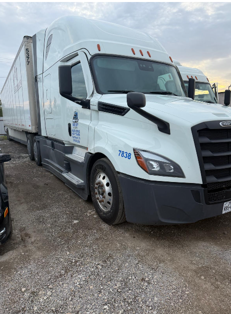 White Freightliner sleeper tractor coupled to a dry trailer, parked on gravel.