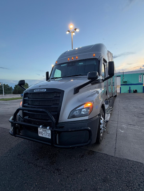 Front view of a silver Freightliner tractor with a black grille guard, parked outdoors.